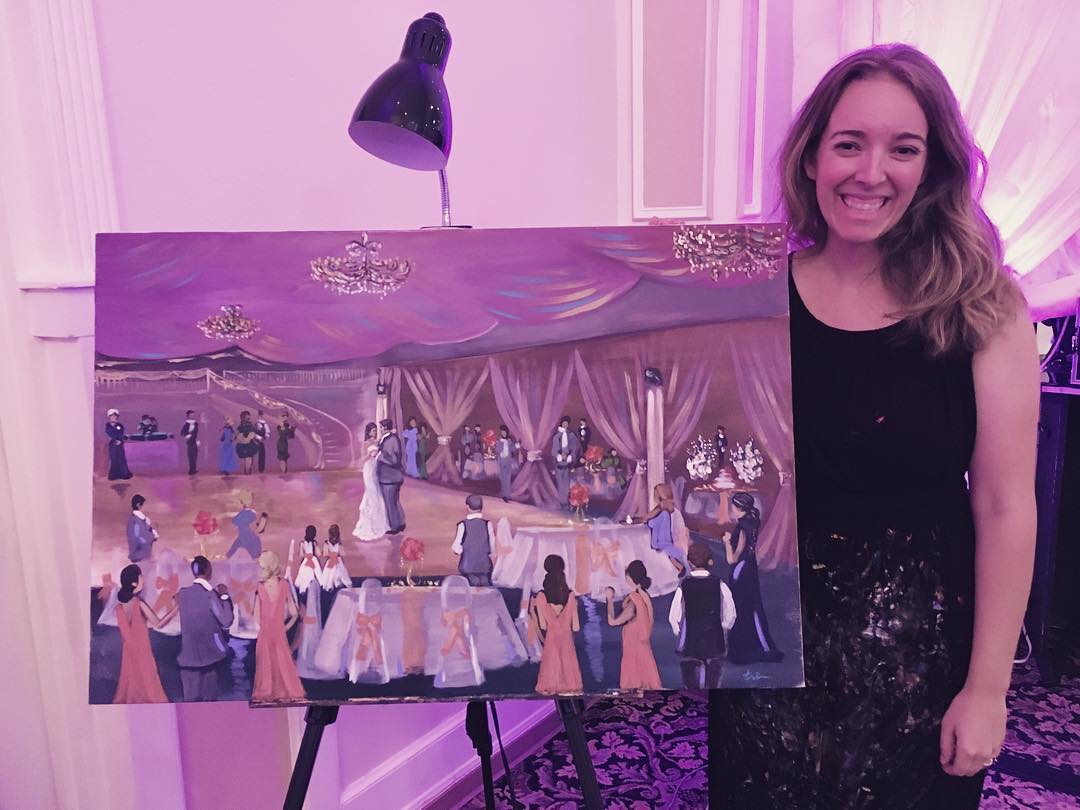 Blaire Brown smiling beside a finished live wedding painting on an easel at a reception